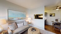 This single-floor residence offers a thoughtfully designed layout that balances functionality with a warm, contemporary aesthetic. The living area serves as the heart of the home, featuring neutral walls, carpeted flooring, and a large window that admits ample natural light. A pass-through opening connects the living space directly to the kitchen, enhancing the sense of openness and ease of movement between rooms.

The kitchen is efficiently arranged in a galley-style configuration, featuring gray cabinetry with clean-lined hardware, light countertops, a stainless steel sink, and black appliances including a refrigerator and electric range. Wood-look flooring grounds the space with a warm contrast to the cabinetry.

The bedroom is a comfortable, carpeted retreat with windows that bring in natural light. It offers sufficient space for a full furniture arrangement, including nightstands on either side of the bed, contributing to a well-balanced, restful atmosphere.

The bathroom includes a vanity with gray cabinetry, a white countertop, a combined tub and shower with a curtain enclosure, and wood-look flooring. The overall palette throughout the residence is cohesive, utilizing soft neutrals and understated finishes to create a calm, livable environment.
