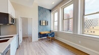 Located at 180 Westminster Street in the heart of Providence, Rhode Island, this single-floor unit blends contemporary design with urban convenience. Throughout the space, light wood-tone flooring creates a clean, cohesive foundation that connects each area seamlessly.

The living and sleeping area serves as the central focus of the unit, highlighted by a bold geometric blue accent wall that adds visual depth and character. Large double-hung windows frame sweeping views of Providence's downtown skyline, allowing abundant natural light to fill the room. A wall-mounted television, desk, and seating area complete the functional layout.

A separate bedroom provides a quieter retreat, also benefiting from oversized windows with city views. The room includes a wall-mounted television, a wood-accented nightstand, and access to ample wardrobe storage via a freestanding white wardrobe unit positioned nearby.

The compact kitchenette is efficiently designed with white cabinetry, a stainless steel refrigerator, built-in microwave, dishwasher, and a single-basin sink — offering all essential conveniences within a streamlined footprint.

The bathroom features large-format dark tile flooring and a full glass-enclosed walk-in shower with overhead rainfall fixture, delivering a clean and modern aesthetic. Overall, the unit presents a well-organized, thoughtfully finished urban living space in a prime downtown Providence location.