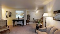 Located at 3220-3224 Mary St in Marinette, Wisconsin, this single-floor property offers a practical and inviting layout designed for comfortable everyday living. The main living area features neutral-toned carpeting that extends throughout, creating a cohesive and warm atmosphere. A ceiling fan with a light fixture provides both comfort and illumination to the open living and dining space, which flow naturally into one another. The dining area accommodates a round table with seating, positioned beneath soft ambient light, while a decorative display cabinet adds a charming touch to the corner. A pass-through window connects the main living space to the kitchen, providing an open sightline and enhancing the sense of connectivity between rooms. The kitchen features warm wood-toned cabinetry and benefits from natural light through a window above the counter. Neutral wall tones throughout the space contribute to a clean, understated aesthetic. The layout is well-suited for both relaxed daily living and casual entertaining, with a smooth and accessible single-level floor plan that makes the entire space easy to navigate.