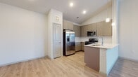 This thoughtfully designed single-floor residence offers a cohesive blend of modern finishes and functional living spaces. The open-concept kitchen is a standout feature, showcasing taupe shaker-style cabinetry, a full suite of stainless steel appliances including a French door refrigerator, electric range, and built-in microwave, complemented by light quartz countertops and a peninsula with an undermount sink. Elegant pendant lighting hangs above, while light-toned hardwood-style flooring flows seamlessly throughout the main living areas. Vaulted ceilings in the kitchen and adjoining living space lend an airy, expansive feel, further enhanced by a ceiling fan and a window that invites natural light. The bedrooms are carpeted for comfort, each equipped with a ceiling fan and windows that provide outdoor views. A spacious walk-in closet with wire shelving offers generous storage capacity. The primary bathroom features a sleek glass-enclosed walk-in shower with tile surround, a single-sink vanity, and wood-look flooring. A second full bathroom includes a soaking tub with shower combination, over-cabinet storage, and a wide vanity with a white countertop. The overall ambiance is clean, bright, and move-in ready.