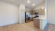 This thoughtfully designed single-floor residence offers a cohesive blend of modern finishes and functional living spaces. The open-concept kitchen is a standout feature, showcasing taupe shaker-style cabinetry, a full suite of stainless steel appliances including a French door refrigerator, electric range, and built-in microwave, complemented by light quartz countertops and a peninsula with an undermount sink. Elegant pendant lighting hangs above, while light-toned hardwood-style flooring flows seamlessly throughout the main living areas. Vaulted ceilings in the kitchen and adjoining living space lend an airy, expansive feel, further enhanced by a ceiling fan and a window that invites natural light. The bedrooms are carpeted for comfort, each equipped with a ceiling fan and windows that provide outdoor views. A spacious walk-in closet with wire shelving offers generous storage capacity. The primary bathroom features a sleek glass-enclosed walk-in shower with tile surround, a single-sink vanity, and wood-look flooring. A second full bathroom includes a soaking tub with shower combination, over-cabinet storage, and a wide vanity with a white countertop. The overall ambiance is clean, bright, and move-in ready.
