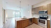 Located at 4150 Ashford Dunwoody Rd NE in Brookhaven, GA, this thoughtfully designed one-bedroom, one-bathroom residence offers a contemporary living experience with modern finishes throughout. The open-concept layout seamlessly connects the kitchen and living room, creating a bright and functional shared space. Light wood-style flooring flows through the main living areas, enhancing the clean, modern aesthetic.

The kitchen is a standout feature, equipped with warm wood cabinetry, quartz countertops, a peninsula island with a double sink, stainless steel appliances — including a refrigerator, range, microwave, and dishwasher — pendant lighting, and a stone tile backsplash. The living area is bathed in natural light from large sliding glass doors that open onto a private balcony with exterior views.

The bedroom is carpeted for comfort, features a ceiling fan, and is served by a generously sized walk-in closet with full wire shelving systems for ample storage. The bathroom is well-appointed with wood-toned cabinetry, a quartz vanity, a tub-shower combination with marble-style tile surround, and neutral tile flooring. The overall ambiance of the space is clean, bright, and move-in ready.