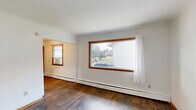 Located at 2080 Coon Rapids Blvd NW in Coon Rapids, Minnesota, this two-bedroom, one-bathroom unit offers a compact and functional single-floor layout designed to make the most of every square foot. Warm wood-tone trim and accents carry consistently throughout the space, complemented by durable hardwood-style flooring that unifies the rooms with a cohesive, clean aesthetic.

The kitchen is outfitted with honey-toned wood cabinetry spanning both upper and lower sections, providing ample storage. A double stainless steel sink, laminate countertops, and a white electric range with an overhead ventilation hood complete the cooking space, keeping it practical and efficient.

The primary bedroom is the largest of the two rooms, featuring a wide picture window framed in warm wood that allows natural light to fill the space. A closet with a sliding wood-panel door adds convenient storage. The second bedroom also benefits from natural light, with two wood-framed windows offering views of the surrounding greenery. Both rooms are serviced by baseboard heating.

The bathroom includes a wood-vanity with a large mirror cabinet, a white countertop sink, and a shower-tub combination. Warm white walls throughout the unit keep the overall ambiance bright and welcoming, while the consistent use of warm wood finishes creates a unified and inviting character across the entire space.