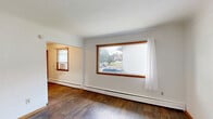 Located at 2080 Coon Rapids Blvd NW in Coon Rapids, Minnesota, this two-bedroom, one-bathroom unit offers a compact and functional single-floor layout designed to make the most of every square foot. Warm wood-tone trim and accents carry consistently throughout the space, complemented by durable hardwood-style flooring that unifies the rooms with a cohesive, clean aesthetic.

The kitchen is outfitted with honey-toned wood cabinetry spanning both upper and lower sections, providing ample storage. A double stainless steel sink, laminate countertops, and a white electric range with an overhead ventilation hood complete the cooking space, keeping it practical and efficient.

The primary bedroom is the largest of the two rooms, featuring a wide picture window framed in warm wood that allows natural light to fill the space. A closet with a sliding wood-panel door adds convenient storage. The second bedroom also benefits from natural light, with two wood-framed windows offering views of the surrounding greenery. Both rooms are serviced by baseboard heating.

The bathroom includes a wood-vanity with a large mirror cabinet, a white countertop sink, and a shower-tub combination. Warm white walls throughout the unit keep the overall ambiance bright and welcoming, while the consistent use of warm wood finishes creates a unified and inviting character across the entire space.