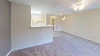 Located on Starling Lane in Durham, NC, this single-floor residence offers a practical and comfortable layout designed for everyday living. The open-concept living and dining area is generously sized, finished with soft wall-to-wall carpeting and bathed in natural light from large windows with slatted blinds. A decorative ceiling light fixture adds a welcoming touch to the main living space. The kitchen features a pass-through counter that opens directly to the living and dining areas, creating a connected and social flow throughout the home. It is equipped with white appliances including a refrigerator, stovetop, and oven, complemented by light wood cabinetry and ample counter space. A pendant light fixture above the pass-through adds a subtle design accent. The living area extends to a private balcony through a set of sliding glass doors, offering outdoor views of lush, mature tree coverage — an inviting retreat for relaxing or entertaining. A ceiling fan with integrated lighting in the main room provides both comfort and functionality. The bathroom is well-appointed with a single-sink vanity featuring a white countertop, wood-toned cabinetry, a large mirror, a tub-shower combination, and wood-look vinyl flooring. Throughout the space, neutral tones and clean finishes create a bright, cohesive, and move-in-ready environment.