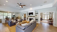 Located at 112 Stonemill Dr in Lynchburg, Virginia, this single-floor home combines modern farmhouse aesthetics with a warm, inviting atmosphere. The open-concept layout connects the main living area, dining space, and kitchen seamlessly, creating a generous and cohesive flow throughout.

The living room serves as the heart of the home, anchored by a brick fireplace framed with built-in shelving and topped with a mounted television. Recessed lighting and ceiling fans complement the tray ceiling details, while large windows flood the space with natural light and offer views of the surrounding greenery. Light hardwood flooring runs throughout, adding warmth and continuity.

Sliding barn doors add a charming farmhouse touch, connecting adjoining rooms with character and style. A cozy sitting area near a bank of windows provides a bright nook, perfect for relaxing and enjoying the outdoor views.

The kitchen features crisp white shaker cabinetry, quartz countertops, a large island with a matte black farmhouse sink, and stainless steel appliances. A casual dining area nearby, bathed in natural light from oversized windows, offers a welcoming spot for everyday meals. The overall design palette of soft greens, whites, and natural wood tones creates a calm, cohesive aesthetic throughout the entire home.