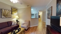 This single-story, 3-bedroom, 2-bathroom home offers a thoughtfully designed layout that maximizes both comfort and functionality. The living area is generously sized, featuring warm hardwood flooring that extends throughout the main living spaces, creating a cohesive and inviting atmosphere. Crown molding accents the ceilings, adding a refined architectural detail, while a ceiling fan provides year-round comfort. The living room offers ample space for seating arrangements and is complemented by neutral-toned walls that provide a versatile backdrop for a variety of décor styles.

A half-wall partition separates the living area from the kitchen, creating a semi-open concept feel while maintaining distinct zones for living and cooking. The kitchen features built-in shelving with glass-front upper sections, offering both storage and display options. A long hallway connects the main living areas to the three bedrooms and two bathrooms, with consistent hardwood flooring and clean white baseboards running throughout.

The textured ceilings and well-placed lighting fixtures ensure each area is well-lit and functional. Overall, this home presents a practical yet comfortable single-floor living experience with classic finishes and a warm, welcoming ambiance throughout.