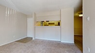 This single-floor residence offers a practical and well-organized layout connecting living, sleeping, and functional spaces. The living area is generously sized and finished with neutral-toned carpet, providing a comfortable foundation for furnishings. A defining architectural feature is the built-in pass-through opening that connects the living area to the kitchen, framed by white cabinetry above and a counter-height partition below, creating an open yet defined separation between the two spaces.

The kitchen is efficiently arranged with white cabinetry, light-toned countertops, and wood-look tile flooring. Black appliances, including an electric range and dishwasher, are positioned along the walls, and a window above the sink area allows natural light to brighten the space.

The bedrooms are carpeted and feature ceiling fans with integrated lighting. Each room includes windows fitted with blinds, allowing adjustable natural light. One bedroom includes a mirrored sliding closet, while another connects to a walk-in closet area.

Two bathrooms serve the unit. One features a vanity with drawer storage and wood-look flooring, while the other includes a full tub-shower combination with white tile surround. Both bathrooms maintain a clean, neutral aesthetic consistent with the rest of the space.