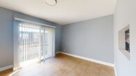 Located in West Palm Beach, Florida, this single-floor unit offers a clean, functional layout finished consistently throughout with warm-toned ceramic tile flooring and soft blue-gray painted walls trimmed in crisp white baseboards. The open living and dining areas are bright and welcoming, with large sliding glass doors dressed in vertical blinds that invite natural light and provide access to an outdoor area. Additional living spaces are served by well-placed windows that frame views of the surrounding greenery.

The galley-style kitchen is efficiently designed, featuring white cabinetry with brushed hardware, granite-patterned countertops, a stainless gas range with overhead ventilation, and a full-size refrigerator. A dedicated exterior door in the kitchen adds convenient direct access.

The bedrooms are comfortably sized, each with its own closet — including a reach-in closet with a full-width rod and a separate room featuring a bifold-door closet. Ceiling vents throughout indicate central air conditioning for year-round comfort in the Florida climate.

The bathroom showcases floor-to-ceiling marble-look tile surrounding a soaking tub with chrome fixtures, lending a clean and polished aesthetic. The overall layout, as seen in the dollhouse view, is compact yet well-organized, making efficient use of every area.