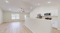 This single-story home offers a thoughtfully designed layout across three bedrooms, two bathrooms, and a variety of functional spaces. The open-concept kitchen and living area serves as the heart of the home, featuring vaulted ceilings with recessed lighting and a ceiling fan that enhance the sense of spaciousness. The kitchen is outfitted with crisp white cabinetry, stainless steel appliances including a refrigerator, range, and microwave, and a peninsula that provides additional counter space and separates the cooking area from the living room. Natural light flows in through multiple windows, brightening the neutral-toned interiors throughout. Light wood laminate flooring runs consistently across all rooms, tying the spaces together with a clean, modern aesthetic. The primary bedroom is generously sized and includes a walk-in closet with wire shelving for ample storage. The bathrooms feature white vanities with modern hardware and light wood-toned flooring that maintains the home's cohesive palette. A dedicated laundry room includes washer and dryer hookups. A hallway connects the bedrooms and bathrooms efficiently. The attached garage provides additional storage and parking, equipped with an automatic opener. Three closets throughout the home ensure practical storage solutions at every turn.