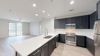 Located at 8910 Southwestern Blvd in Dallas, Texas, this single-floor residence showcases a clean, modern design with thoughtfully selected finishes throughout. The open-concept kitchen serves as a central highlight, featuring dark navy cabinetry with brushed hardware, crisp white quartz countertops, a subway tile backsplash, and a full suite of stainless steel appliances including a gas range, built-in microwave, dishwasher, and refrigerator. A peninsula with an undermount sink and a sleek pull-down faucet extends the workspace while connecting seamlessly to the adjacent living area, which is finished with light wood-style flooring and recessed lighting. The bedrooms are carpeted for comfort, with one room offering direct access to a private balcony through sliding glass doors and a ceiling fan overhead. Generous closet space is present, including a walk-in closet with built-in shelving and hanging rods. The bathrooms are well-appointed, with one featuring a soaking tub and shower combo surrounded by white square tile, and another offering a separate glass-enclosed shower stall alongside a navy vanity with a wide mirror and white countertop. Light wood-style flooring carries through the bathrooms and hallways, maintaining a cohesive aesthetic across the entire unit.