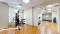 Located at 544 Birchmount Road in Toronto's Scarborough district, this single-floor fitness facility offers a thoughtfully organized workout environment across two dedicated exercise rooms. The space features warm hardwood flooring throughout the open areas, complemented by a drop-panel ceiling with recessed lighting that creates a bright, welcoming atmosphere.

The first exercise room serves as a versatile open-concept area, ideal for movement-based activities. Its clean, cream-colored walls are accented with vibrant artwork, and a glass-paneled door provides convenient access to the exterior. The spacious layout offers ample room for dynamic workouts, martial arts training, or group exercise sessions.

The second exercise room is purpose-built for strength and cardio training. It houses a multi-station cable machine, two modern treadmills, a stationary cycle, adjustable weight benches, and an ab/back extension station. Rubber flooring mats are strategically placed beneath the equipment for safety and stability, while large windows with vertical blinds invite natural light and outdoor views. Wall-mounted instructional charts and mirrors further enhance the functional design.

Together, the two rooms form a comprehensive and well-maintained fitness facility suited for a range of training needs, from cardiovascular conditioning to strength development.