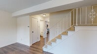 This thoughtfully laid-out multi-floor home spans three levels, offering a functional and comfortable living arrangement. The main level features a living room and a combined dining and kitchen area. The kitchen is well-appointed with white shaker-style cabinetry, granite countertops, a peninsula breakfast bar, hardwood-style flooring, and black appliances including a refrigerator, range, microwave, and dishwasher. A window allows natural light to brighten the space.

The upper floor houses both bedrooms, each featuring plush carpeting, ceiling fans with light fixtures, and windows with views of surrounding greenery. The primary bedroom includes dual closets with built-in shelving and hanging rods, providing generous storage. A second family room is also present, along with a carpeted bonus room on the lower level that is well-suited for flexible use.

The two bathrooms offer distinct finishes — one features a granite-topped vanity with a dark-framed mirror and mosaic tile accents, while the other includes a full tub and shower combination with clean white tile surround and hardwood-style flooring. Throughout the home, a decorative staircase with white metal balusters connects all three levels, adding a charming architectural detail to the interior.