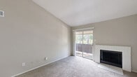 Located at 407 Greens Rd in Houston, TX, this single-story, one-bedroom, one-bathroom unit offers a well-organized layout across a comfortable footprint. The living room is the standout space, featuring dramatic vaulted ceilings that lend an open, airy feel. A tile-surround wood-burning fireplace anchors one wall, while a sliding glass door on the opposite side allows natural light to pour in and provides a view of the greenery beyond. Carpet flooring runs throughout the living and bedroom areas, contributing a warm, quiet atmosphere. A pass-through window connects the living area to the kitchen, which features white cabinetry. A ceiling fan in the adjoining area adds both function and comfort. The bedroom is a generous size with a dedicated closet featuring shelving, and a window that brings in additional natural light. Neutral-toned walls throughout create a clean, versatile canvas. The bathroom is well-appointed with a white vanity topped with a marble-style countertop, a large mirror, wood-look flooring, and a tiled tub-shower combination. A hallway and closet complete the layout, providing practical storage. The unit's design balances simplicity with key architectural details for comfortable everyday living.