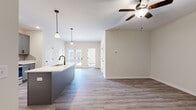 This single-story, one-bedroom, one-bathroom unit offers a thoughtfully designed open-concept layout that maximizes its comfortable footprint. The combined kitchen and living area serves as the heart of the space, where wood-look luxury vinyl plank flooring, neutral beige walls, and a ceiling fan create a bright, cohesive atmosphere. French doors at the far end of the living area invite natural light and provide outdoor access.

The kitchen is well-equipped with gray shaker-style cabinetry, a subway tile backsplash, white quartz countertops, and a full suite of stainless steel appliances including a refrigerator with ice maker, electric range, and over-the-range microwave. A kitchen island with a built-in sink and pendant lighting above adds both workspace and visual interest.

The bedroom is a generously sized, carpeted retreat with a ceiling fan, a window offering natural light, and access to a dedicated closet. The bathroom features a blue-gray vanity with white countertop, a wall-mounted light fixture, a full tub and shower combination, and wood-look flooring that ties back to the main living areas. The overall design is clean, modern, and move-in ready.