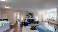 This single-floor residence offers a thoughtfully designed layout that balances comfort and functionality throughout. The open-concept living area serves as the heart of the home, featuring rich hardwood-style flooring, a textured ceiling, and warm neutral-toned walls. The living room provides generous space for lounging and entertaining, flowing seamlessly into a dedicated dining area and a bright den or office nook lined with large windows that frame outdoor greenery and invite abundant natural light, complemented by a ceiling fan overhead.

The galley-style kitchen is outfitted with warm wood cabinetry, granite-style countertops, a deep stainless sink, and black appliances including a refrigerator and range, making it a practical and efficient cooking space.

Two well-proportioned bedrooms offer a peaceful retreat, each carpeted for added comfort. The primary bedroom features soft, warm lighting and ample room for a full furniture arrangement, while the second bedroom mirrors the same calm ambiance.

Two full bathrooms serve the residence, each featuring wood-style flooring, vanities with granite-style countertops, and tub-shower combinations. The overall design is cohesive and neutral, creating a welcoming and versatile living environment throughout.