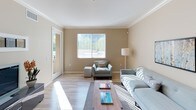 This single-floor residence offers a thoughtfully designed layout with a cohesive neutral palette of warm beige and taupe tones carried throughout each room. The living area is bright and welcoming, featuring light hardwood-style flooring, crown molding, and large windows with vertical blinds that allow abundant natural light to filter in. A sliding glass door provides direct access to an outdoor balcony, extending the living space seamlessly.

The kitchen is well-equipped, showcasing rich dark-stained cabinetry, granite countertops, stainless steel appliances including a gas range and built-in microwave, and a breakfast bar that connects to the dining area. The adjacent dining space features light hardwood flooring and a pendant light fixture overhead.

The bedrooms are carpeted and comfortably sized, each offering generous closet space. One bedroom features sliding glass door access to the balcony, while another includes a dedicated workspace area with dual windows. The primary bathroom features an extended dark-wood vanity with double sinks, granite countertops, a large mirror, and walk-in closet access. Additional bathrooms offer tub-shower combinations, tile flooring, and built-in shelving for added storage convenience.