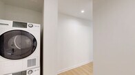 Located on the 10th floor of 351 Marin Blvd in Jersey City's vibrant waterfront district, this one-bedroom, one-bathroom residence offers a well-designed layout with a clean, contemporary aesthetic throughout. Light wood flooring runs continuously across the open-plan kitchen and living area, lending warmth and cohesion to the space.

The modern kitchen is a standout feature, outfitted with stainless steel appliances including a full-size refrigerator, electric range, and built-in microwave. Sleek gray cabinetry extends to the ceiling for ample storage, complemented by a quartz countertop island with an undermount sink. Large floor-to-ceiling windows frame striking views of the Jersey City skyline, flooding the space with natural light.

The living area continues the open, airy feel with expansive corner windows offering panoramic city views, creating an inviting and light-filled environment. The bedroom is a comfortable, well-proportioned room with its own large window overlooking the surrounding cityscape and light wood flooring throughout.

The bathroom is finished with large-format neutral floor tiles, a soaking tub, a wood-toned vanity with integrated sink, and a mirrored medicine cabinet, all set against clean white walls for a crisp, modern feel.
