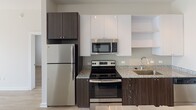Located at 430 E 36th St in Charlotte, NC, this single-floor residence combines modern design with functional living spaces throughout. The open-concept layout connects the kitchen and dining area seamlessly, creating an inviting flow ideal for everyday living and entertaining.

The kitchen is outfitted with stainless steel appliances, including a refrigerator, electric range, and built-in microwave. Granite countertops sit atop two-tone cabinetry featuring dark wood lower cabinets paired with crisp white upper cabinets and open shelving. Light wood-style flooring runs throughout the common areas, adding warmth and continuity.

The dining area benefits from track lighting and a pendant fixture, while a built-in bar ledge adds a contemporary touch. The living room is bright and airy, with sliding glass doors leading to a private balcony overlooking a landscaped courtyard.

Two bedrooms are present, each with ceiling fans, natural light from windows, and distinct storage solutions — one featuring frosted sliding closet doors and another with a classic barn-style sliding door. A hallway area provides additional storage with wire shelving, and a bathroom with clean, neutral finishes completes the layout.