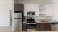 Located at 430 E 36th St in Charlotte, NC, this single-floor residence combines modern design with functional living spaces throughout. The open-concept layout connects the kitchen and dining area seamlessly, creating an inviting flow ideal for everyday living and entertaining.

The kitchen is outfitted with stainless steel appliances, including a refrigerator, electric range, and built-in microwave. Granite countertops sit atop two-tone cabinetry featuring dark wood lower cabinets paired with crisp white upper cabinets and open shelving. Light wood-style flooring runs throughout the common areas, adding warmth and continuity.

The dining area benefits from track lighting and a pendant fixture, while a built-in bar ledge adds a contemporary touch. The living room is bright and airy, with sliding glass doors leading to a private balcony overlooking a landscaped courtyard.

Two bedrooms are present, each with ceiling fans, natural light from windows, and distinct storage solutions — one featuring frosted sliding closet doors and another with a classic barn-style sliding door. A hallway area provides additional storage with wire shelving, and a bathroom with clean, neutral finishes completes the layout.