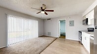 This well-organized single-floor unit offers a practical and comfortable layout across its thoughtfully designed rooms. The combined kitchen and living area serves as the heart of the space, where light wood-style flooring runs throughout. The kitchen is outfitted with crisp white shaker-style cabinetry, light stone countertops, and a full suite of stainless steel appliances including a refrigerator, electric range, dishwasher, and microwave — providing a clean, modern aesthetic. The living area transitions seamlessly from the kitchen, featuring plush carpet, a ceiling fan with integrated lighting, and a large sliding glass door dressed with vertical blinds that fills the room with natural light and offers outdoor views. The bedroom is a comfortable, carpeted retreat with its own ceiling fan, a large window with vertical blinds providing additional natural light, and direct access to a dedicated closet. The full bathroom features a tiled shower-tub combo with clean white finishes and wood-style flooring. Textured ceilings are consistent throughout the unit, adding a classic residential character. Overall, the space presents a clean, functional, and well-appointed layout suited for efficient everyday living.