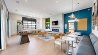 Located in Melissa, TX, this well-appointed single-floor community clubroom offers a thoughtfully designed gathering space that blends modern aesthetics with comfortable functionality. The open-plan layout is anchored by bold teal accent walls that contrast beautifully against crisp white surfaces, light wood-look flooring, and soaring ceilings that amplify the sense of openness throughout.

The main lounge area features a striking patterned tile feature wall housing a wall-mounted flat-screen TV above a sleek linear electric fireplace, creating an inviting focal point. Curated seating arrangements—including warm cognac leather chairs, upholstered lounge sofas, and bistro-style high-top tables—offer flexible spaces for socializing or relaxing. A foosball table adds a recreational element to the space.

The kitchen area is outfitted with white shaker cabinetry, white quartz countertops, stainless steel appliances, and an oversized black-framed window wall that floods the space with natural light and offers views of the surrounding community.

Floor-to-ceiling sliding glass doors open directly onto a covered outdoor patio overlooking a resort-style pool, seamlessly connecting the interior to the exterior. Pendant lighting, gallery wall art, and carefully selected décor throughout complete the polished, contemporary ambiance of this vibrant community space.