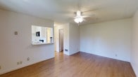 This single-floor studio presents an open, versatile layout designed to maximize functionality. The main living area features warm hardwood flooring that extends throughout, creating a cohesive and inviting atmosphere. A ceiling fan with an integrated light fixture is centrally mounted on the textured ceiling, providing both air circulation and ambient lighting.

The kitchen is thoughtfully positioned along one wall and opens to the main living space via a pass-through counter, promoting an open feel while maintaining a clear distinction between the cooking and living zones. The kitchen is equipped with a range and a microwave mounted above it, along with white cabinetry that contributes to a bright, clean aesthetic.

A doorway visible from the main living area leads to an additional space, likely a bathroom or closet, adding to the unit's practicality. The neutral white walls throughout the space offer a blank canvas, allowing for flexible interior styling. A floor vent ensures efficient climate control. Overall, the studio maintains a simple, tidy ambiance suited to comfortable everyday living.