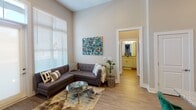 Located at 1–31 N Center St in downtown Hickory, North Carolina, this single-floor unit offers a thoughtfully designed layout with a clean, contemporary aesthetic throughout. Notably high ceilings elevate the sense of space across every room, allowing natural light to flow generously through large, blind-fitted windows.

The living area is a welcoming, open space anchored by wide-plank hardwood-style flooring, tall windows that invite abundant daylight, and direct access to the unit's entrance via a glass-paneled door with transom window above. The room connects visibly to the bathroom and other areas, reinforcing the unit's open, flowing floor plan.

The kitchen is well-appointed with crisp white shaker cabinetry reaching toward the tall ceilings, granite-style countertops, a subway tile backsplash, and a full suite of stainless steel appliances including a side-by-side refrigerator, electric range, and over-range microwave.

The bedrooms feature plush carpeting, tall ceilings, and large windows providing natural light and outdoor views. Each bedroom is complemented by a bathroom finished with granite countertops, white cabinetry, and wood-look flooring. A dedicated walk-in closet with wire shelving provides practical storage. The unit's neutral color palette and modern finishes create a cohesive, polished ambiance throughout.