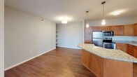 Unit 319 is a single-floor residence thoughtfully designed to balance function and comfort throughout its layout. The kitchen serves as a central highlight, outfitted with warm-toned wood cabinetry, granite countertops, a subway tile backsplash, and a full suite of stainless steel appliances including a refrigerator, range, microwave, and dishwasher. Rich hardwood flooring grounds the kitchen and extends into the adjacent dining area, where a granite-topped island provides additional prep and seating space. The open layout connects seamlessly to the spacious living area, which transitions to soft, neutral carpeting and features large windows fitted with blinds that invite natural light.

The bedrooms are carpeted and generously sized, each with windows offering outdoor views and ample wall space. The unit includes two full bathrooms, both finished with tile flooring, a tub-shower combination, toilet, and a dark wood vanity topped with a light countertop. One bathroom also features a well-lit framed mirror above the vanity. A dedicated laundry area houses a full-sized top-load washer and dryer with overhead shelving for added storage. Neutral wall tones throughout create a clean, cohesive aesthetic.