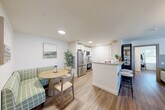 This thoughtfully designed one-bedroom, two-bathroom residence at 1 Ridge Rd in Auburn, Massachusetts offers a comfortable and modern living experience across a well-proportioned single floor. The open-concept kitchen and living area serves as the heart of the home, featuring white shaker cabinetry, granite countertops, stainless steel appliances including a French door refrigerator and range, and a cozy dining nook — all tied together by warm hardwood-style flooring that flows throughout the unit. The living room is anchored by a distinctive board-and-batten accent wall with an elegant oval mirror, creating a refined focal point. A second living area offers additional flexibility, filled with natural light from a large window overlooking the outdoors. The spacious bedroom features dual windows that invite abundant natural light and outdoor views, providing a serene retreat. Both bathrooms are well-appointed with granite vanities and white cabinetry; one includes a full soaking tub with shower. Clean white walls, consistent flooring, and a neutral palette lend the space a cohesive, modern aesthetic throughout.