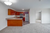 This single-floor residence offers a thoughtfully designed layout that balances comfort and functionality throughout. The kitchen is a standout feature, equipped with rich cherry wood cabinetry, light stone-look countertops, stainless steel appliances including a refrigerator, range, and microwave, and tile flooring. A peninsula counter extends the workspace and provides a natural transition into the adjoining living area. The open living space is generously sized, finished with plush neutral carpeting, and features a wall-mounted mini-split HVAC unit for climate control. Sliding glass doors open to a balcony, flooding the room with natural light and offering views of the surrounding greenery. The bedrooms are carpeted and bright, each with windows fitted with blinds that frame outdoor tree views. One bedroom includes a well-organized reach-in closet with shelving and hanging rods. The full bathroom is finished with large-format tile flooring, a wood-toned vanity with a single sink, a wall-mounted mirror with overhead lighting, and a glass-enclosed shower. A dedicated laundry area houses a stacked washer and dryer unit, adding everyday convenience. Warm neutral tones and clean lines throughout give the space a calm, welcoming ambiance.