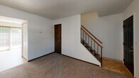 Located at 1462 E College Ave in Normal, IL, this two-story home offers a practical and straightforward layout across two levels. The main floor welcomes you through a bold dark front door into a spacious, carpeted living area filled with natural light from a large multi-pane window. A staircase with a wood handrail and metal balusters leads to the upper level. The galley-style kitchen is outfitted with warm oak cabinetry, ample counter space, a double basin sink, and white appliances including a refrigerator and gas range, all set on tile flooring. A full bathroom on the main level features tile flooring, a vanity with wood cabinetry, and a shower-tub combination. Upstairs, the carpeted bedrooms are bright and well-proportioned, each with windows fitted with blinds that allow natural light to filter in. One bedroom includes a generously sized closet with louvered doors. An additional full bathroom on the upper level mirrors the main floor bath in style and finishes. Throughout the home, dark wood door trim and baseboards provide a consistent design element that complements the neutral white walls and light carpet, creating a clean and functional living environment.