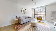 Located at 358 Orange St in New Haven's Audubon neighborhood, this contemporary single-floor unit offers a thoughtfully designed layout with modern finishes throughout. The kitchen is a standout feature, equipped with stainless steel appliances including a gas range, microwave, and French door refrigerator. Dark espresso cabinetry contrasts elegantly with bright white quartz countertops and a classic subway tile backsplash. A peninsula with seating for two, accented by striking gold wire chairs, provides both functionality and style. Pendant lighting and polished concrete flooring complete the kitchen's modern aesthetic. The open living area is bathed in natural light from large floor-to-ceiling windows that frame views of the surrounding neighborhood. Track lighting overhead and warm hardwood-style flooring create an inviting atmosphere well-suited for both relaxing and entertaining. The bedroom is a serene retreat, featuring plush carpeting, generous natural light from a large sliding glass door that opens to a private balcony, and ample closet space. Neutral wall tones and clean architectural lines carry throughout the unit, contributing to a cohesive and contemporary feel. A bathroom with wood-look tile flooring connects seamlessly to the rest of the layout, rounding out this well-appointed urban residence.