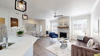 This thoughtfully designed one-bedroom, one-bathroom residence offers a cohesive open-concept floor plan that maximizes every inch of its single-story layout. The combined kitchen and living area serves as the heart of the home, anchored by a striking chevron-patterned tile fireplace flanked by two large windows that fill the space with natural light. A ceiling fan overhead and warm wood-look flooring throughout the main living areas contribute to a comfortable, modern atmosphere.

The kitchen is a standout feature, showcasing bright white shaker cabinetry, a classic subway tile backsplash, and an expansive white quartz peninsula with an undermount sink. Stainless steel appliances—including a refrigerator, range, and microwave—complete the space, while two geometric pendant lights add an industrial-chic touch. A dedicated dining area sits adjacent, offering a natural transition between cooking and entertaining spaces.

The bedroom is a generously sized, carpeted retreat with a ceiling fan and access to a walk-in closet. The full bathroom is clean and functional, featuring a soaking tub and shower combination with white tile surround and ample cabinetry. Additional conveniences include two closets and a dedicated laundry area, making this a complete and practical living space.