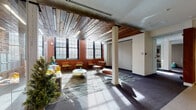 Located at 275 Winchester Ave in New Haven, CT, this single-floor amenity space masterfully combines industrial heritage with contemporary design. The expansive lounge area serves as the centerpiece, featuring striking reclaimed wood plank ceilings, exposed brick walls, and large multi-pane windows that flood the space with natural light. Eclectic seating — including tufted leather chairs and colorful benches — is arranged atop a patterned area rug, while sculptural art pieces lend a gallery-like quality to the open layout. Structural columns throughout add to the building's original character.

A glass-walled conference room offers transparency and connectivity, furnished with a long meeting table and ergonomic chairs, and framed by views of the sunlit lounge. Adjacent corridors feature light wood-toned flooring, clean white walls, and curated artwork, leading to a welcoming nook with built-in shelving, a teal accent wall, and a wall-mounted display panel.

The fitness center is well-equipped with cardio machines, a cable weight station, stationary bikes, and a weight bench, all set against exposed brick walls and hardwood floors bathed in natural light. A casual lounge and social area rounds out the floor, offering high-top tables, bar stools, and wall-mounted flat-screen TVs — ideal for informal gatherings.