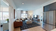 This single-floor residence offers a well-designed open-concept layout that seamlessly connects the kitchen, dining, and living areas. The kitchen is a standout feature, equipped with slate-blue cabinetry, stainless steel appliances, white subway tile backsplash, under-cabinet lighting, open shelving, and a white quartz island with bar seating—ideal for both cooking and entertaining. Light wood-style flooring runs throughout the main living areas, enhancing the bright and airy atmosphere.

The living room accommodates multiple seating arrangements and benefits from generous natural light through large windows dressed with sheer curtains. A dedicated sitting nook near the windows provides additional functional space with urban views.

Both bedrooms feature plush carpet, ceiling fans, roller shades, and large windows that frame city views. Each bathroom is finished with slate-blue vanity cabinetry, white quartz countertops, and clean white walls. One bathroom includes a shower-tub combination, while the other features a walk-in shower.

A dedicated laundry area with a full-size washer and dryer adds everyday convenience. The overall design maintains a cohesive contemporary aesthetic with a neutral palette accented by blue tones throughout.