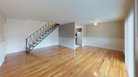 This two-story residence is defined by warm hardwood flooring that runs consistently throughout both levels, creating a cohesive and inviting atmosphere. The main level opens into a spacious living area featuring large sliding glass doors fitted with vertical blinds, allowing generous natural light and outdoor views of surrounding greenery. A staircase with a sleek metal railing connects the levels, and an adjacent dining or secondary living space features exposed brick detailing and a ceiling fan, adding character to the layout.

The kitchen is efficiently designed with warm wood cabinetry, a dark mosaic tile backsplash, granite-style countertops, and stainless steel appliances including a gas range and refrigerator. The black-and-white patterned tile flooring adds a classic touch to the space.

Upstairs, the bedrooms are bright and generously sized, each with polished hardwood floors and natural light from windows. One bedroom includes a closet with built-in shelving, while another features a wall-mounted air conditioning unit. The bathroom is cleanly appointed with a vanity, mirror cabinet, and a combined tub and shower enclosure, completing this functional and well-maintained residence.
