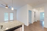 This single-floor residence is designed with a clean, contemporary aesthetic and a functional open-concept layout. The kitchen serves as a central hub of the unit, equipped with dark espresso cabinetry, a subway tile backsplash, stainless steel appliances including a refrigerator, range, microwave, and dishwasher, and a granite-topped peninsula with an undermount sink and pendant lighting overhead. The peninsula connects seamlessly to the adjacent living and dining areas, promoting an open and connected flow throughout the space.

The living area features hardwood-style flooring, white walls, and a ceiling fan, with French doors that open to an outdoor area, allowing for natural light and exterior access. The bedrooms are carpeted for comfort, each with ceiling fans, natural light from multiple windows with blinds, and closet storage. One bedroom benefits from a particularly bright corner layout with two windows.

The bathroom includes hardwood-style flooring, a dark vanity with granite countertop, a large mirror, and contemporary lighting fixtures. Throughout the unit, consistent finishes—granite surfaces, dark cabinetry, and neutral tones—create a cohesive and polished living environment.