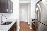 Located at 380 Prospect Ave in Hackensack, NJ, this well-appointed single-floor residence offers a clean, modern aesthetic throughout. Rich hardwood-style flooring flows seamlessly across the living areas and bedrooms, creating a warm and cohesive feel. The spacious living room is bathed in natural light through large windows and features sliding glass doors that open onto a private balcony, offering pleasant outdoor views and a seamless indoor-outdoor connection. The kitchen is thoughtfully designed with dark espresso cabinetry, granite-style countertops, and stainless steel appliances including a refrigerator, range, and dishwasher. A window at the end of the kitchen corridor adds additional natural light to the space. The bedrooms are generously proportioned, each featuring large windows that invite ample daylight, with one bedroom also offering built-in closet storage. The unit includes two updated bathrooms, both finished with a consistent design palette: dark wood vanities with white basin sinks, large framed mirrors with overhead lighting, neutral tile wainscoting, and classic hexagonal tile flooring. One bathroom includes a glass-enclosed shower, while the other offers additional storage cabinetry. The overall ambiance is bright, clean, and move-in ready.