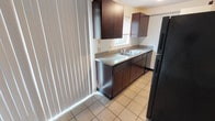 This two-story residence offers a practical and well-organized layout across both floors. The main level welcomes you through a front entry door into a spacious living area finished with rich, dark hardwood flooring that extends throughout. Large vertical blinds frame the front windows, allowing natural light to fill the room, while baseboard heating runs along the walls. A staircase with a railing leads to the upper floor, seamlessly connecting both levels.

The kitchen is thoughtfully designed with dark espresso-toned cabinetry — both upper and lower — paired with granite-style countertops and a double basin sink positioned beneath a window. Tile flooring carries through this space, and a black refrigerator anchors one end of the kitchen. Vertical blinds provide additional light control.

Upstairs, the bedrooms are carpeted throughout, offering a soft and comfortable feel. Each room is well-lit by windows, including one with a view of mature trees outside. Baseboard heaters are present in the bedrooms as well. The upper-level hallway connects the bedrooms to a bathroom featuring a vanity with a white countertop and an adjacent water closet with tile flooring. Closet space is accessible from the hallway, adding to the functional design of the upper floor.