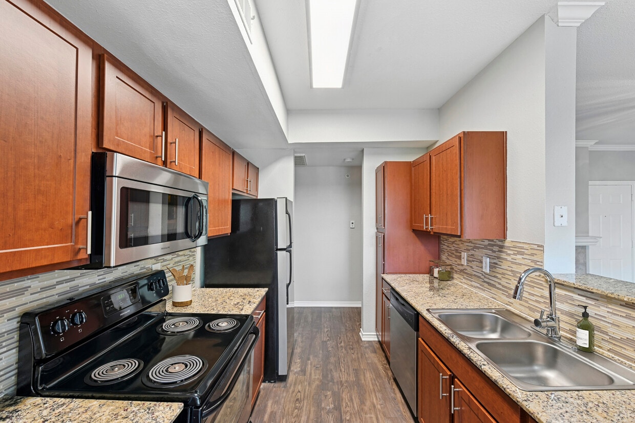 Kitchen with chestnut cabinetry, speckled granite countertops, tile backsplash, stainless steel appliances, and hard surface flooring - eaves North Dallas