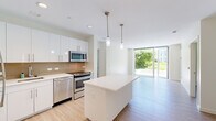 Located at 199 N Harvard St, Unit S204 in Boston's Allston neighborhood, this modern 2-bedroom, 2-bathroom residence offers a thoughtfully designed single-level layout. Light wood-style flooring flows throughout, complementing the clean, contemporary aesthetic of the space.

The open-concept kitchen is a standout feature, outfitted with sleek white cabinetry, a tile backsplash, stainless steel appliances including a refrigerator, dishwasher, range, and microwave, as well as a central island with quartz countertops and pendant lighting overhead. The kitchen flows seamlessly into the living area, which is bathed in natural light from expansive floor-to-ceiling sliding glass doors that open to an outdoor patio with greenery views.

The primary bedroom is generously sized and also features large sliding glass doors providing direct outdoor access and lush tree views. The second bedroom includes a window overlooking the surrounding landscape, offering a bright and airy feel. Both rooms feature the same light hardwood-style flooring found throughout the unit.

The two bathrooms are clean and modern: one features a glass-enclosed walk-in shower with white subway tile and an LED-backlit vanity mirror, while the second includes a full tub and shower combination with matching tile finishes and white cabinetry.