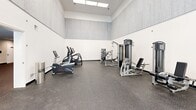 Located at 3223 Arrowhead Circle in Fairfax, Virginia, this fitness center offers a generously sized, single-floor layout divided into two distinct exercise rooms designed to support a comprehensive workout experience. The facility is thoughtfully designed with durable rubber flooring throughout, providing both safety and comfort during exercise.

The first exercise room is notably expansive, featuring soaring ceilings with large skylights that flood the space with natural light. Textured upper walls add a modern architectural detail, while the open floor plan accommodates a variety of strength and cardio machines, including ellipticals, treadmills, stair climbers, cable machines, and weight benches.

The second exercise room presents a more intimate setting, accented by a soothing blue-gray color palette and large windows that overlook the outdoor pool area, bringing in abundant natural light and outdoor views. This room is equipped with free weights, a dumbbell rack, medicine balls, kettlebells, and a weight bench. Full-length mirrors line one wall, enhancing the sense of space and supporting proper form during workouts. Recessed lighting and a wall-mounted television add to the functionality and comfort of the space.

Together, the two rooms create a versatile and well-appointed fitness center suited for a wide range of training styles and fitness goals.