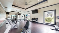 Located at 2400 Briarwest Blvd in Houston, Texas, this dedicated fitness center offers a spacious, single-floor layout designed to support a comprehensive workout experience. The room features a striking tray ceiling with dark trim accents and a large ceiling fan, contributing to both visual appeal and ventilation. Recessed lighting throughout ensures the space remains bright and functional at any hour.

A bold, large-scale typographic mural dominates one wall, featuring fitness-themed words such as "Intensity," "Endurance," and "Performance," creating an energizing and motivational atmosphere. Multiple large windows line the walls, allowing generous natural light to flow in and offering views of the surrounding greenery.

The facility is well-stocked with a diverse range of equipment, including treadmills, elliptical trainers, stationary and spin bikes, a multi-station cable machine, a rowing machine, and a dedicated free weights area with a full dumbbell rack. Exercise balls and medicine balls add additional versatility for functional training. Wall-mounted televisions are positioned throughout for entertainment during workouts.

The durable dark rubber flooring provides safety and comfort underfoot, while the open layout ensures ample room to move freely between equipment stations, making this fitness center a practical and motivating environment for residents.