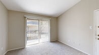 This single-floor residence offers a clean, functional layout finished throughout in warm neutral tones that create a bright and welcoming atmosphere. The kitchen is a standout feature, outfitted with crisp white shaker-style cabinetry with matte black hardware, light wood-look luxury vinyl plank flooring, white countertops, and stainless steel appliances including a refrigerator, electric range, and dishwasher. The galley-style configuration maximizes storage and workspace efficiency. Adjacent to the kitchen, a dedicated dining area is illuminated by a classic pendant light fixture and continues the wood-look flooring. The living spaces are carpeted in a soft, neutral tone, lending comfort underfoot and a cohesive feel throughout. Multiple bedrooms are well-proportioned, each featuring plush carpet, natural light from windows with blinds, and ample wall space. One bedroom includes a ceiling fan with light fixture, adding to everyday comfort. A spacious room opens directly to an outdoor area through a full sliding glass door dressed with vertical blinds, allowing abundant natural light and convenient outdoor access. The overall design is practical and move-in ready, with consistent finishes and a calm, neutral color palette that suits a variety of furnishing styles.