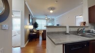This single-floor residence offers a thoughtfully designed layout that balances comfort and functionality across its key living spaces. The open-concept kitchen flows seamlessly into the living area, creating an inviting, connected atmosphere. The kitchen is outfitted with rich dark wood cabinetry, gray countertops, black appliances including a refrigerator, stove, and dishwasher, and warm hardwood flooring that continues into the main living areas. A peninsula counter with additional workspace connects the kitchen to the rest of the home.

The living room is bright and welcoming, featuring crown molding, a ceiling fan with light fixture, and a glass-paneled exterior door that allows natural light to fill the space. Hardwood flooring adds warmth and a polished aesthetic throughout.

The residence includes two bedrooms, each carpeted for comfort and featuring ceiling fans, large windows that invite natural light, and access to walk-in or standard closets. Both bathrooms are finished with light tile flooring, warm wood vanities with gray countertops, large mirrors, and a tub-shower combination, providing a clean and practical design. The overall ambiance is neutral and well-maintained, making for a move-in ready living environment.