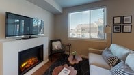 This thoughtfully designed single-floor residence offers a seamless blend of modern comfort and contemporary style throughout its well-appointed rooms. The living area serves as a central gathering space, highlighted by a sleek electric fireplace, wall-mounted television, and large windows with horizontal blinds that invite natural light and provide views of the surrounding neighborhood. Warm hardwood-style flooring runs through the main living areas, enhancing the inviting ambiance.

The kitchen is outfitted with rich, dark espresso cabinetry paired with light quartz countertops, creating a striking contrast. Stainless steel appliances—including a range, microwave, and dishwasher—offer full functionality, while a deep undermount sink adds practicality.

The dining area provides a dedicated space for meals, featuring room for a round table and chairs beneath a pendant light fixture, complemented by wall art that adds a vibrant artistic touch.

The bedroom is a restful retreat with plush carpeting, generous natural light from a large window, and a tufted upholstered headboard as a focal point. A decorative round mirror with a gold frame adds an elegant accent.

The bathroom is finished with dark cabinetry, dual sinks set in light quartz countertops, a large mirror, and a full tub-shower combination, offering both style and functionality.