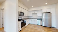 This single-floor unit presents a clean, contemporary design highlighted by light hardwood-style flooring and a neutral white-and-gray color palette carried consistently throughout the space. The open-concept layout connects the living area to the kitchen, creating a sense of spaciousness enhanced by recessed lighting overhead.

The kitchen is well-appointed with white shaker-style cabinetry, gray countertops, and a full suite of stainless steel appliances, including an electric range, over-the-range microwave, dishwasher, and refrigerator. Ample upper and lower cabinetry provides generous storage, while the undermount sink adds a polished, functional touch.

The living area is bright and open, with smooth white walls and recessed lighting that contribute to an airy atmosphere. A bedroom features a window fitted with horizontal blinds, allowing natural light to filter in while maintaining privacy.

Two full bathrooms mirror each other in design, each offering white cabinetry, gray countertops, an undermount sink with brushed nickel fixtures, a large mirror, and a tub-shower combination. A dedicated laundry closet houses a stacked Whirlpool washer and dryer alongside a water heater, providing convenient in-unit utility access.