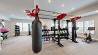 Located at 250 Battery Park Cir in Pendleton, SC, this fitness center offers a thoughtfully designed, single-floor workout space that accommodates a wide variety of training styles. The room is finished with neutral-toned carpet tiles in a herringbone pattern, recessed lighting, and multiple windows fitted with white blinds that allow ample natural light to fill the space.

The strength and functional training zone is anchored by a large multi-station rig in a bold red and black finish, supporting TRX suspension straps, a heavy punching bag, medicine balls, and an extensive dumbbell rack. A dedicated cable machine and weight bench provide additional options for resistance training. A wall-mounted mirror expands the sense of space and supports form-checking during workouts.

The cardio section features treadmills and stationary spin bikes, each positioned near the windows to provide an open, airy feel during use. Rowing machines and additional cardio equipment round out the options. A wall-mounted flat-screen TV is centrally positioned, enhancing the workout experience.

Stability balls, BOSU trainers, resistance tools, and balance equipment are neatly organized along the walls, ensuring the space remains uncluttered and functional. The clean, neutral aesthetic combined with a diverse equipment offering makes this fitness center a comprehensive facility for residents.