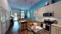 Located at 1133 Commerce Dr in Decatur, GA, this single-floor residence blends modern design with vibrant personality. The open-concept living and kitchen area is anchored by a striking teal accent wall that extends from the kitchen through the living space, creating a cohesive and energetic atmosphere throughout.

The kitchen is well-appointed with stainless steel appliances, including a French-door refrigerator, electric range, built-in microwave, and dishwasher. Light wood-grain cabinetry reaches toward the tall ceilings, maximizing storage, while granite countertops and a white subway tile backsplash add a polished, contemporary finish. A peninsula with a sink and matching granite top offers additional prep space and casual seating.

The living area is warm and inviting, featuring dark hardwood-style flooring and large windows dressed with patterned curtains that allow abundant natural light. A cozy reading nook with a leather accent chair sits beside the windows, offering views of the greenery outside.

The bedroom is a calm retreat, carpeted for comfort, with a ceiling fan, natural light from a window, and ample space for a full furniture arrangement. The bathroom includes a tub-shower combo with tile surround, granite vanity, and wood-style flooring, maintaining the same refined material palette found throughout the residence.
